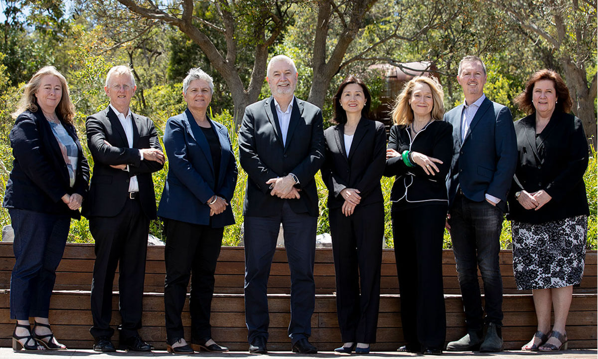 Voluntary board, eight professionals posing outdoors, formal attire, sunny day